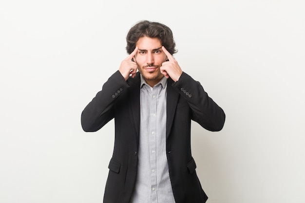 Young business man against a white wall focused on a task, keeping forefingers pointing head.