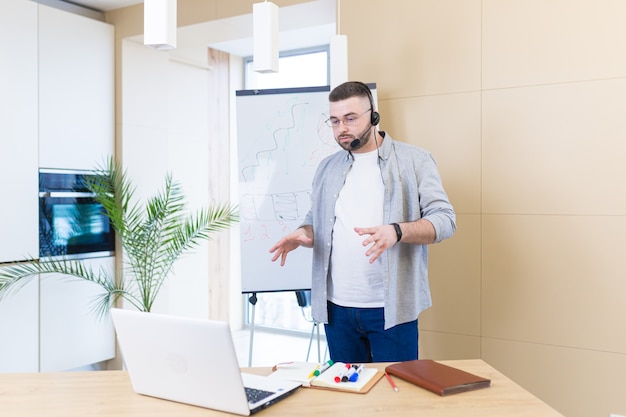 young business man in casual clothes wearing a headset online meeting presentation or training using a laptop webcam and a flipchart