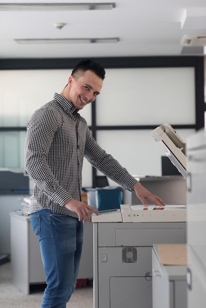 Foto giovane uomo d'affari copia i documenti sulla fotocopiatrice all'interno dell'ufficio di avvio moderno, abbigliamento casual