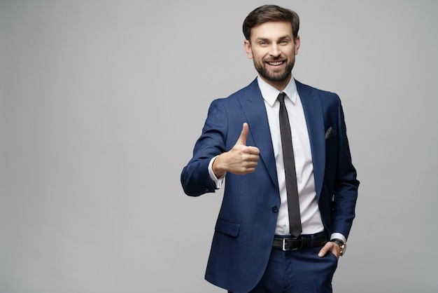 Young business man going thumb up on grey wall