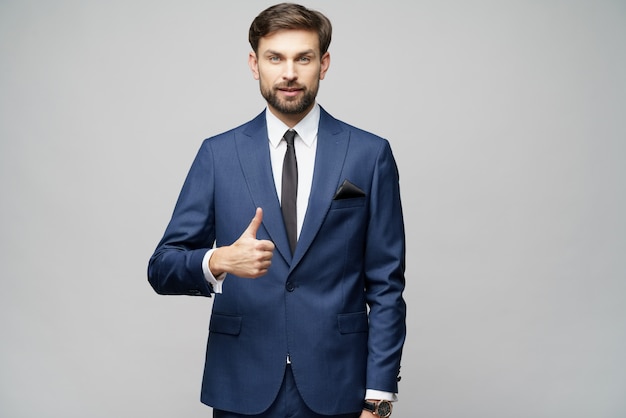 Young business man going thumb up on grey wall