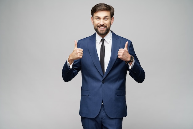 Young business man going thumb up on grey wall