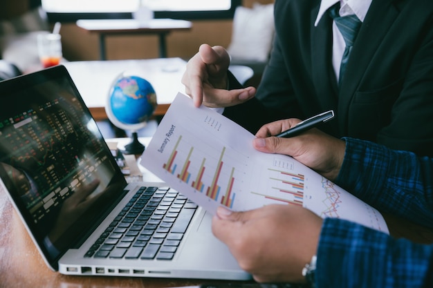 Young business man hand holding pen and pointing graph chart discussing with colleagues about marketing and business progress.