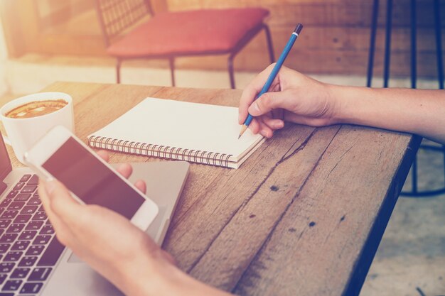 Photo young business man hand holding phone and writing and using laptop in coffee shop with vintage filter.