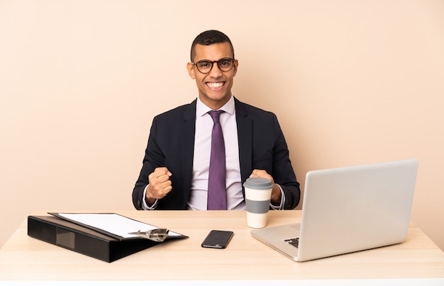 Young business man in his office with a laptop and other documents celebrating a victory in winner position