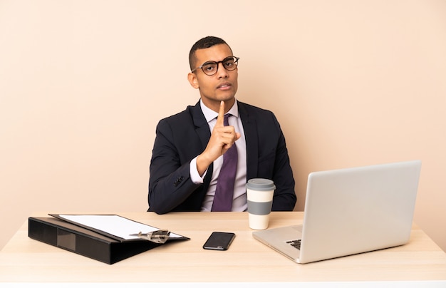 Young business man in his office with a laptop and other documents frustrated and pointing to the front