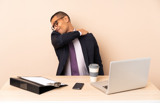 Photo young business man in his office with a laptop and other documents suffering from pain in shoulder for having made an effort