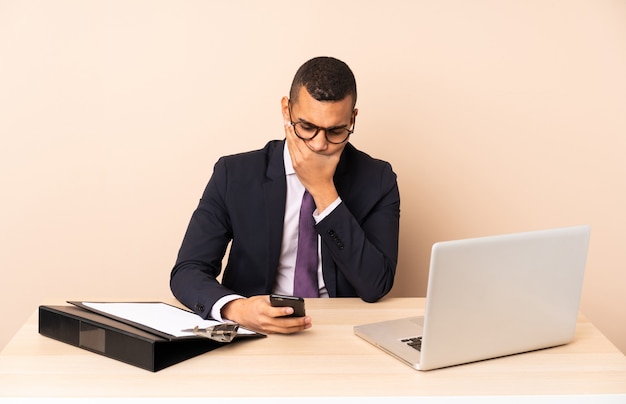 Young business man in his office with a laptop and other documents thinking and sending a message