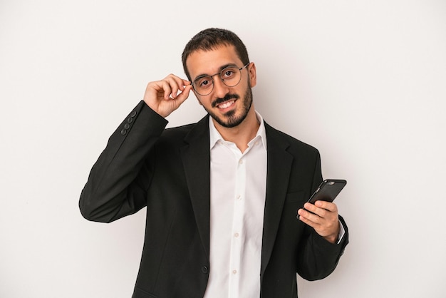 Young business man holding a mobile phone isolated on white background excited keeping ok gesture on eye.