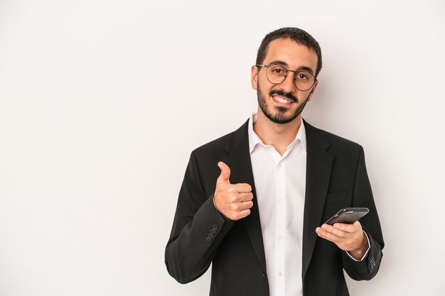 Молодой деловой человек, держащий мобильный телефон, изолированный на белом фоне, улыбается и поднимает палец вверх