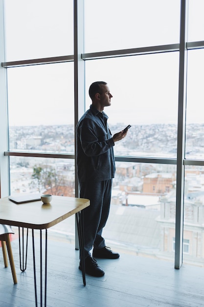 Young business man holding a phone In an office or business center against the background of large windows of a skyscraper Work and career concept