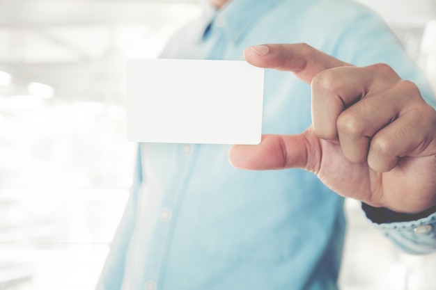 Photo young business man holding white business card on modern office blur background.