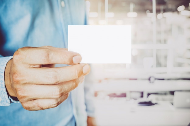 Young business man holding white business card on modern office blur background.