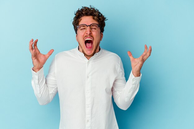 Young business man isolated on blue wall screaming with rage