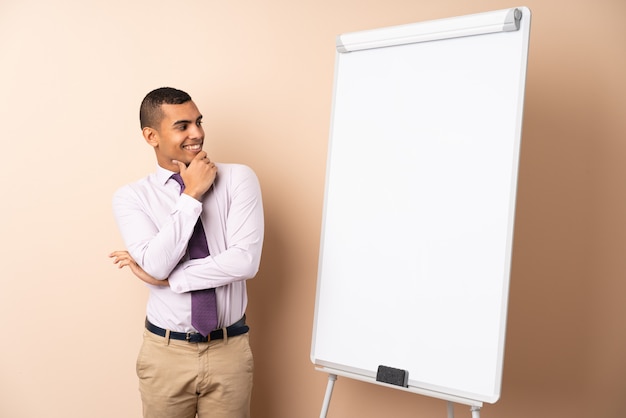 Young business man over isolated wall giving a presentation on white board and looking side