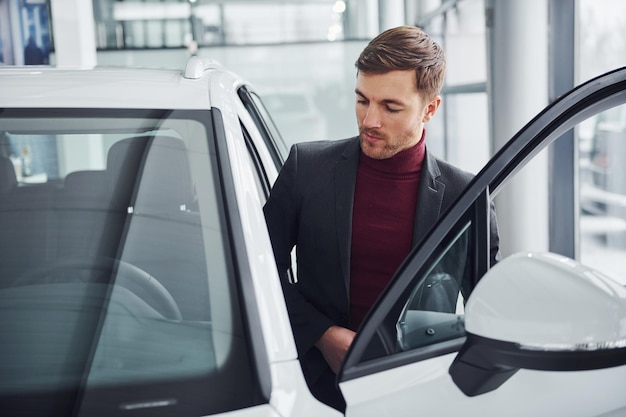 Young business man in luxury suit and formal clothes is indoors near the car.