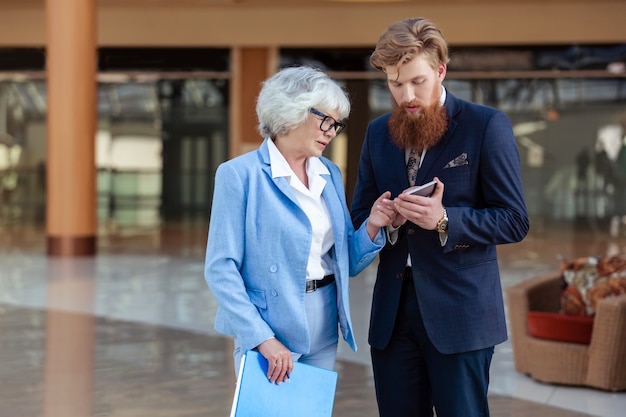 Young business man and senior woman look together at mobile phone