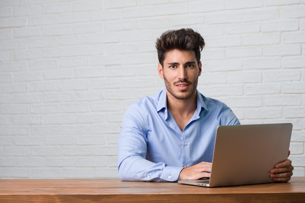 Young business man sitting and working on a laptop crossing his arms, smiling and happy, being confident and friendly