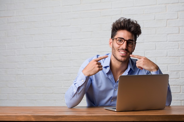 Young business man sitting and working on a laptop smiles, pointing mouth, concept of perfect teeth, white teeth, has a cheerful and jovial attitude