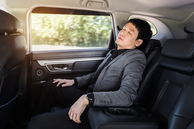 車の後部座席に座って寝ている若いビジネスマン