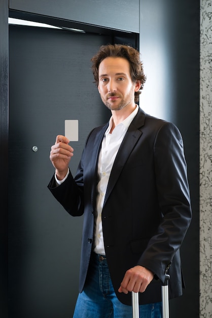 Young business man standing with a keycard in front of a room door in a hotel