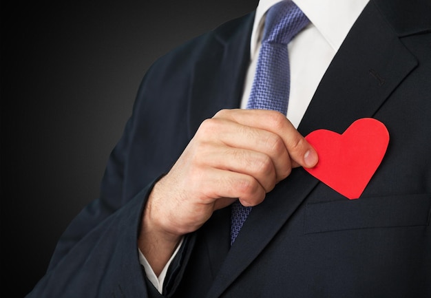 Young business man in suit holding red heart on background