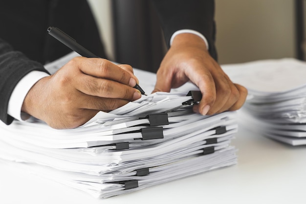 A young business man in a suit is managing paperwork in the\
office. many paperwork that is not finished. documents in the\
company about finance and information of the company.