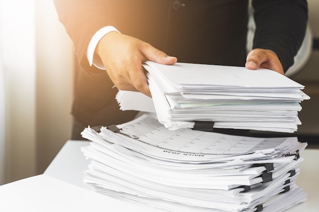 A young business man in a suit is managing paperwork in the
office. many paperwork that is not finished. documents in the
company about finance and information of the company.