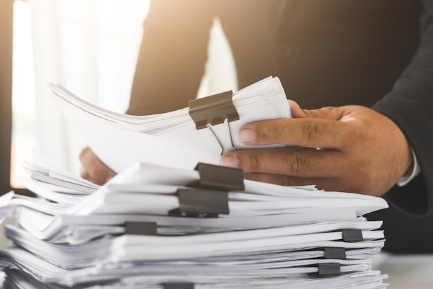 A young business man in a suit is managing paperwork in the office. Many paperwork that is not finished. Documents in the company about finance and information of the company.