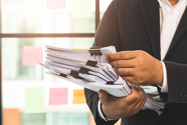 A young business man in a suit is managing paperwork in the
office. many paperwork that is not finished. documents in the
company about finance and information of the company.