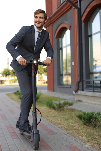 Young business man in suit riding on electric scooter on a business meeting. Ecologic transport concept.