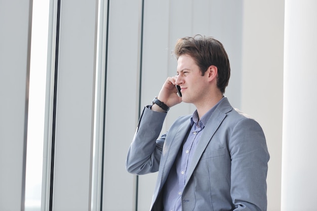 young business man talk by cellphone over bright window in big hall