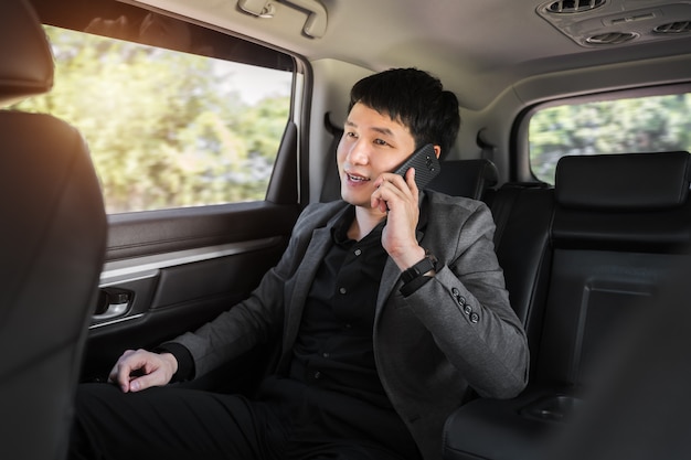 Young business man talking on mobile phone while sitting in the back seat of car