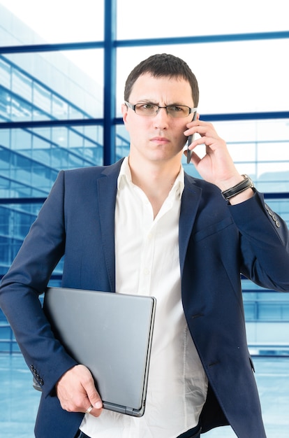 Foto giovane uomo di affari che comunica sul telefono che sembra arrabbiato sopra la priorità bassa delle finestre del grande ufficio