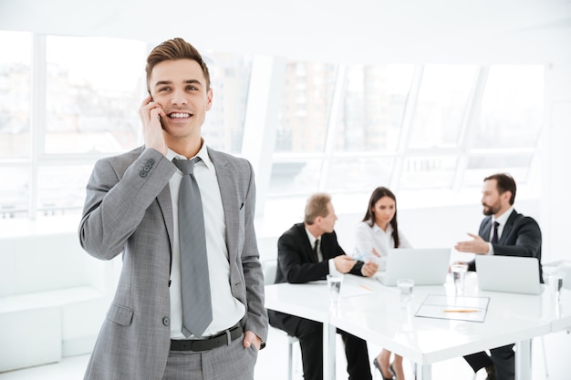 Young Business man talking at phone in office with colleagues by the table