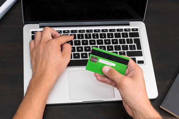 Young business man typing in credit card info on a computer keyboard. Credit card visible in hand. Close up, business office workplace. Debt, paying bills, debit card info, online banking, mortgage