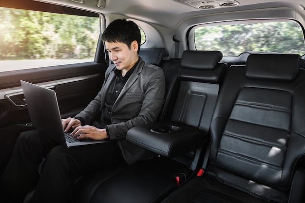 Young business man using laptop computer while sitting in the back seat of car