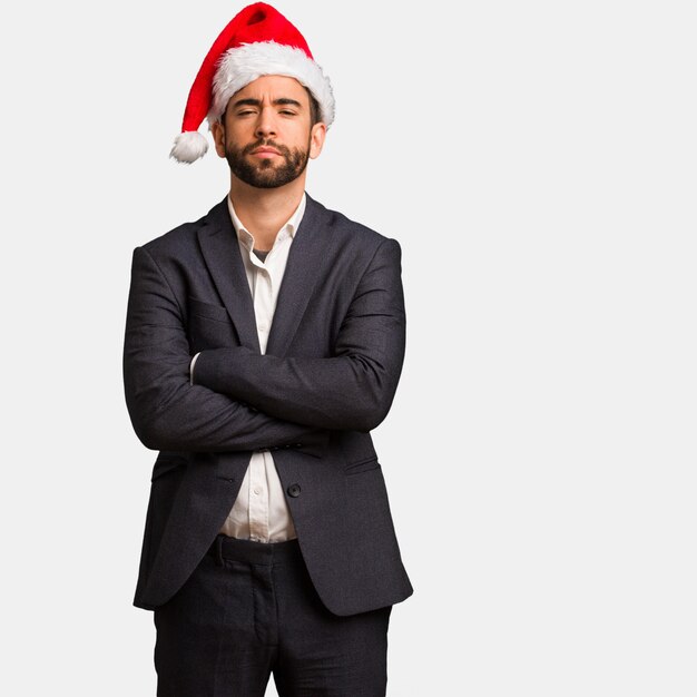 Young business man wearing santa hat crossing arms relaxed