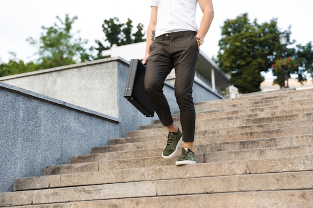 Photo young business man with briefcase walking on stairs with arm in pocket