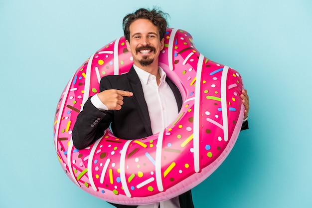 Young business man with inflatable donut isolated on blue background person pointing by hand to a shirt copy space, proud and confident