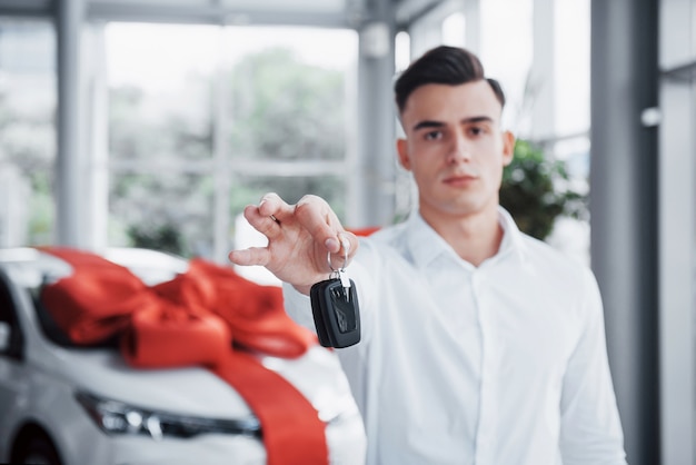 Фото Молодой деловой человек с ключами в руках, покупает машину в салоне.