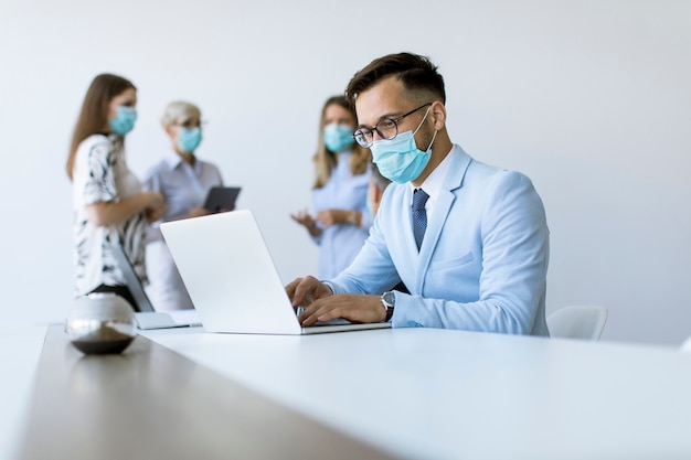 Young business man with medical protective mask works on a laptop in the office