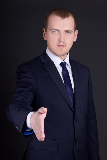 Young business man with open hand ready to handshake over dark background