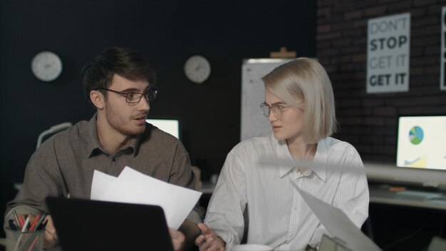 Young business man and woman working together front laptop in dark office