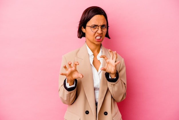 Young business mixed race woman isolated on pink background showing claws imitating a cat, aggressive gesture.