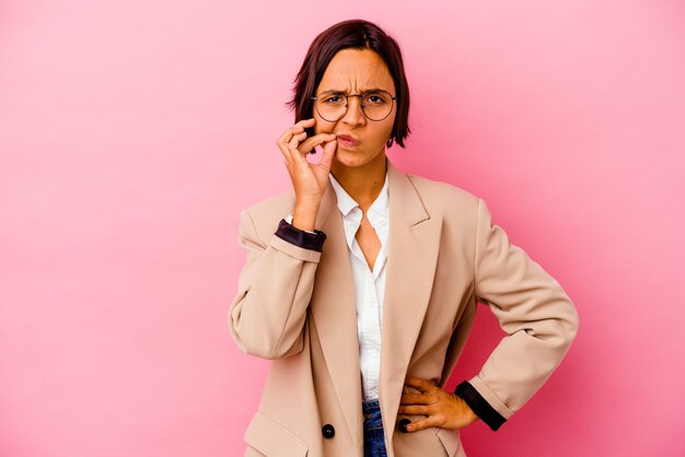 Young business mixed race woman isolated on pink background with fingers on lips keeping a secret.