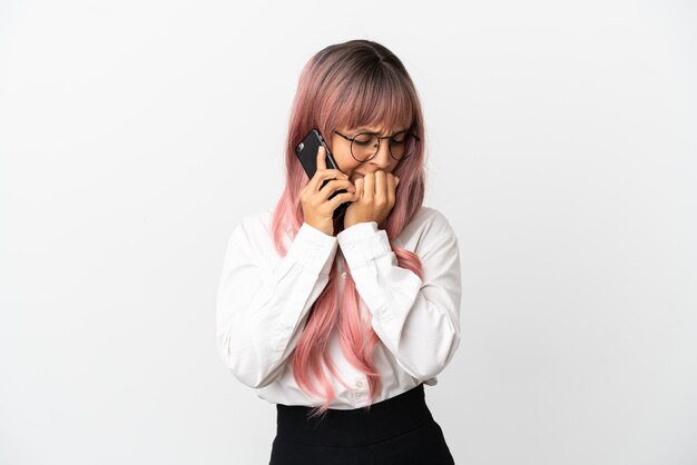 Young business mixed race woman with pink hair holding a mobile isolated on pink background having doubts