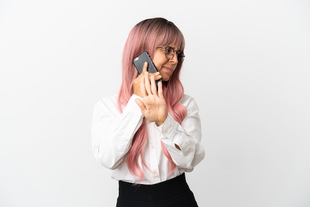 Young business mixed race woman with pink hair holding a mobile isolated on pink background making stop gesture and disappointed