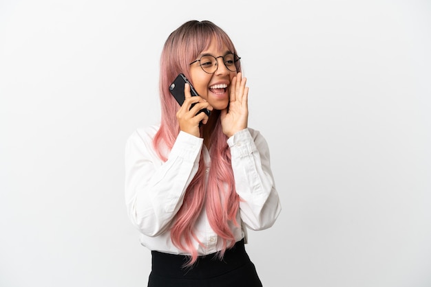 Young business mixed race woman with pink hair holding a mobile isolated on pink background shouting with mouth wide open to the side