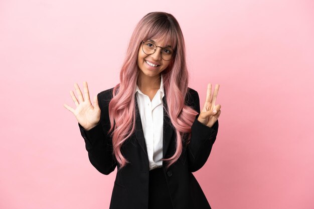 Молодая деловая женщина смешанной расы с розовыми волосами, изолированными на розовом фоне, считает семь пальцами